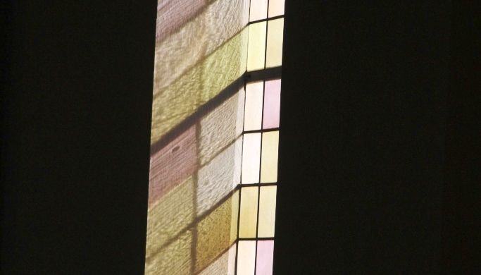 Aufgrund des Sonneneinfalls ergibt sich an der weiÃŸen Wand der Pfarrkirche St. Nikolaus in Hunderdorf das farbliche Spiegelbild der bunten Glasfenster.